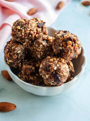 A bowl of cranberry energy balls with almonds scattered around.