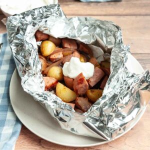 A foil packet filled with sausage and potato, topped with sour cream.