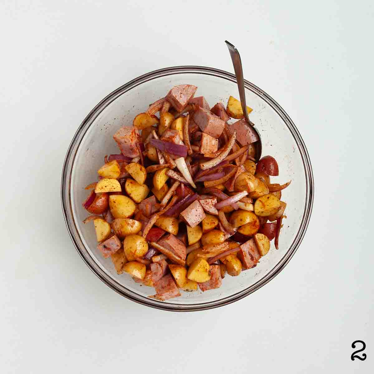 Sausage, potatoes and onion, mixed in a bowl.