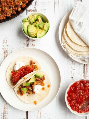 Two tacos with chorizo and potatoes, topped with salsa, sour cream, and avocado.