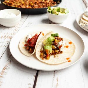Two tacos with chorizo and potatoes, topped with salsa, sour cream, and avocado.