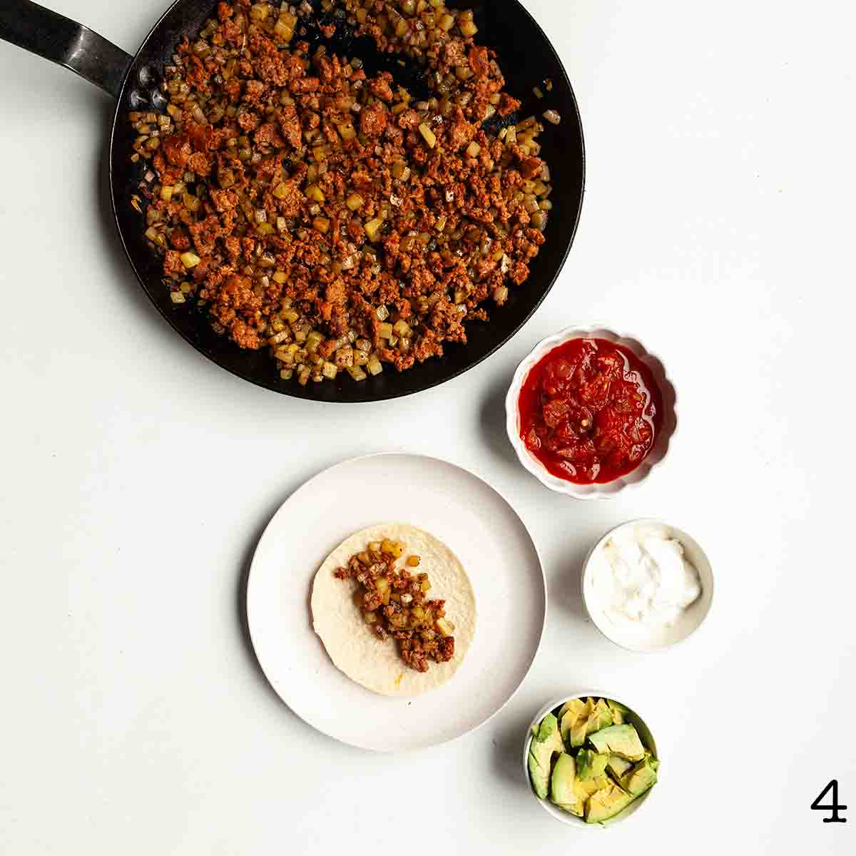 Components to assemble a taco--skillet of meat and potatoes, salsa, sour cream, and avocado.