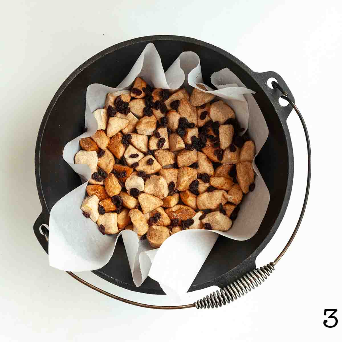 Pieces of biscuit dough and raisins in a parchment-lined Dutch oven.