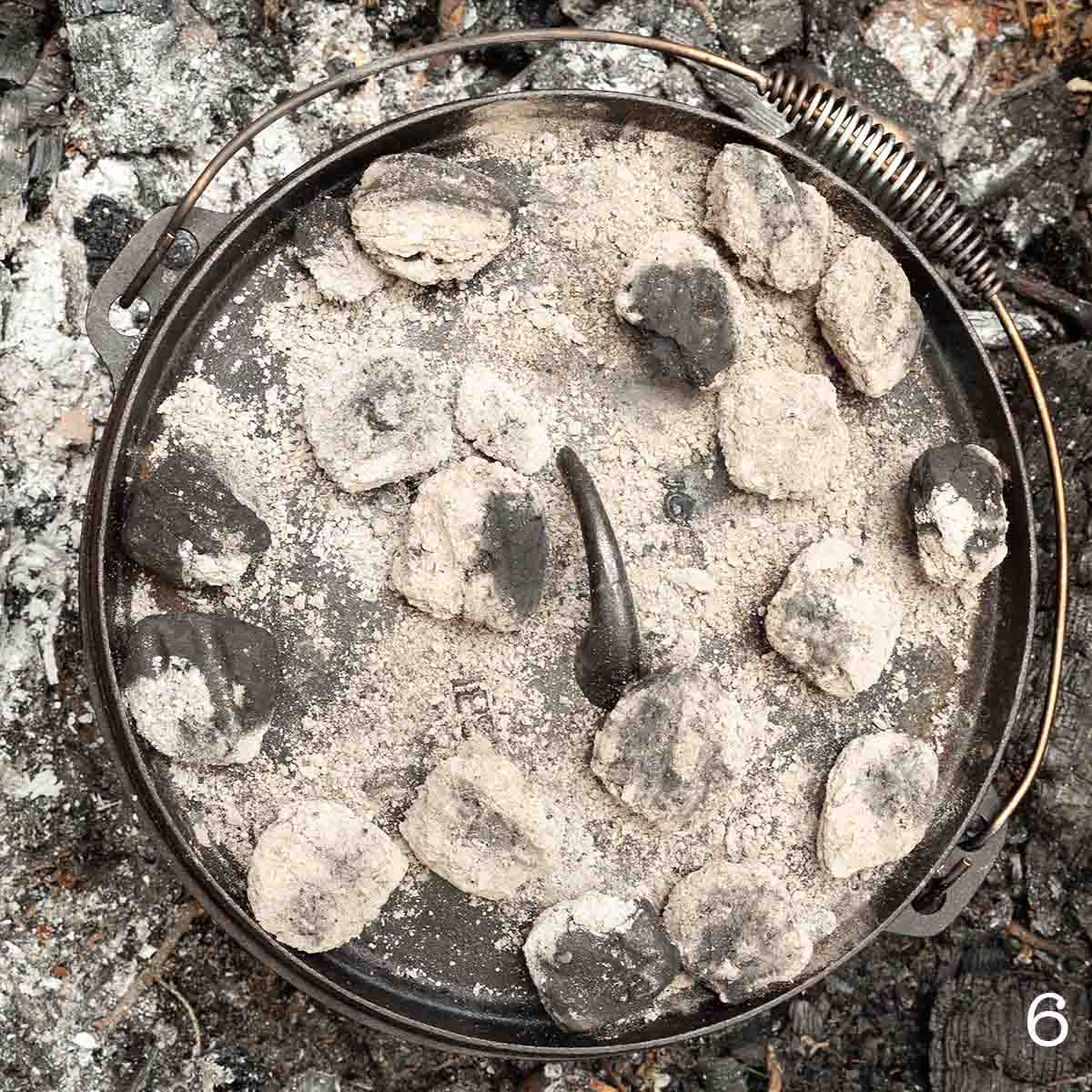 A Dutch oven covered in coals.
