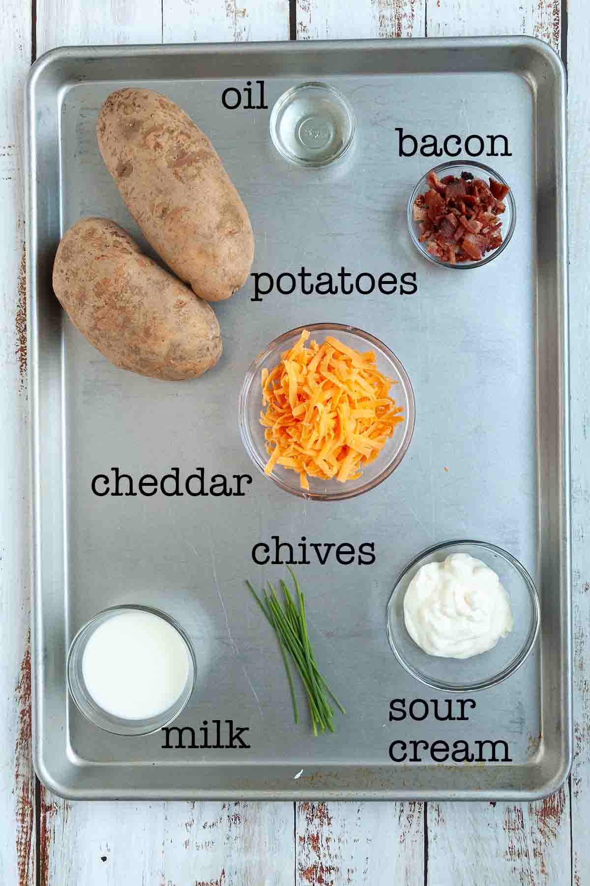 Ingredients for grilled twice-baked potatoes--potatoes, oil, bacon, cheddar, chives, milk, and sour cream.
