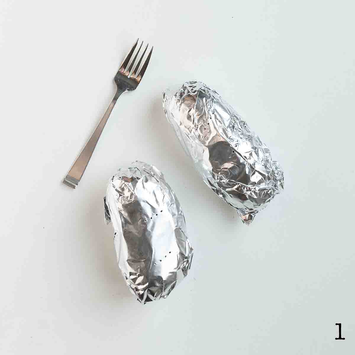 Two potatoes wrapped in foil with a fork on the side.