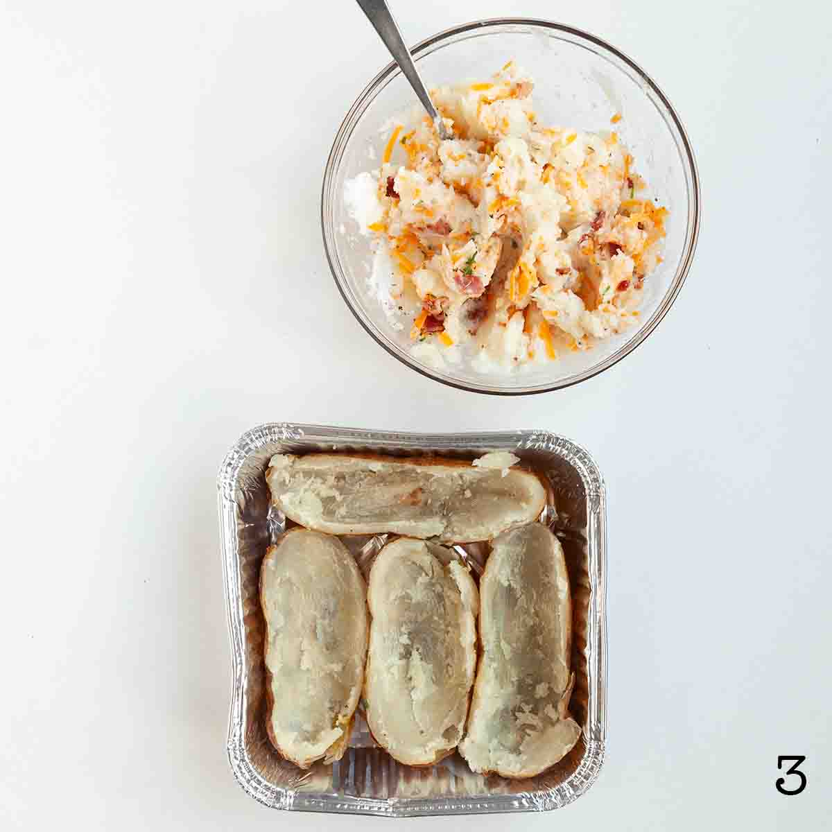 A foil tray with four potato halves and a bowl of mashed potato filling.