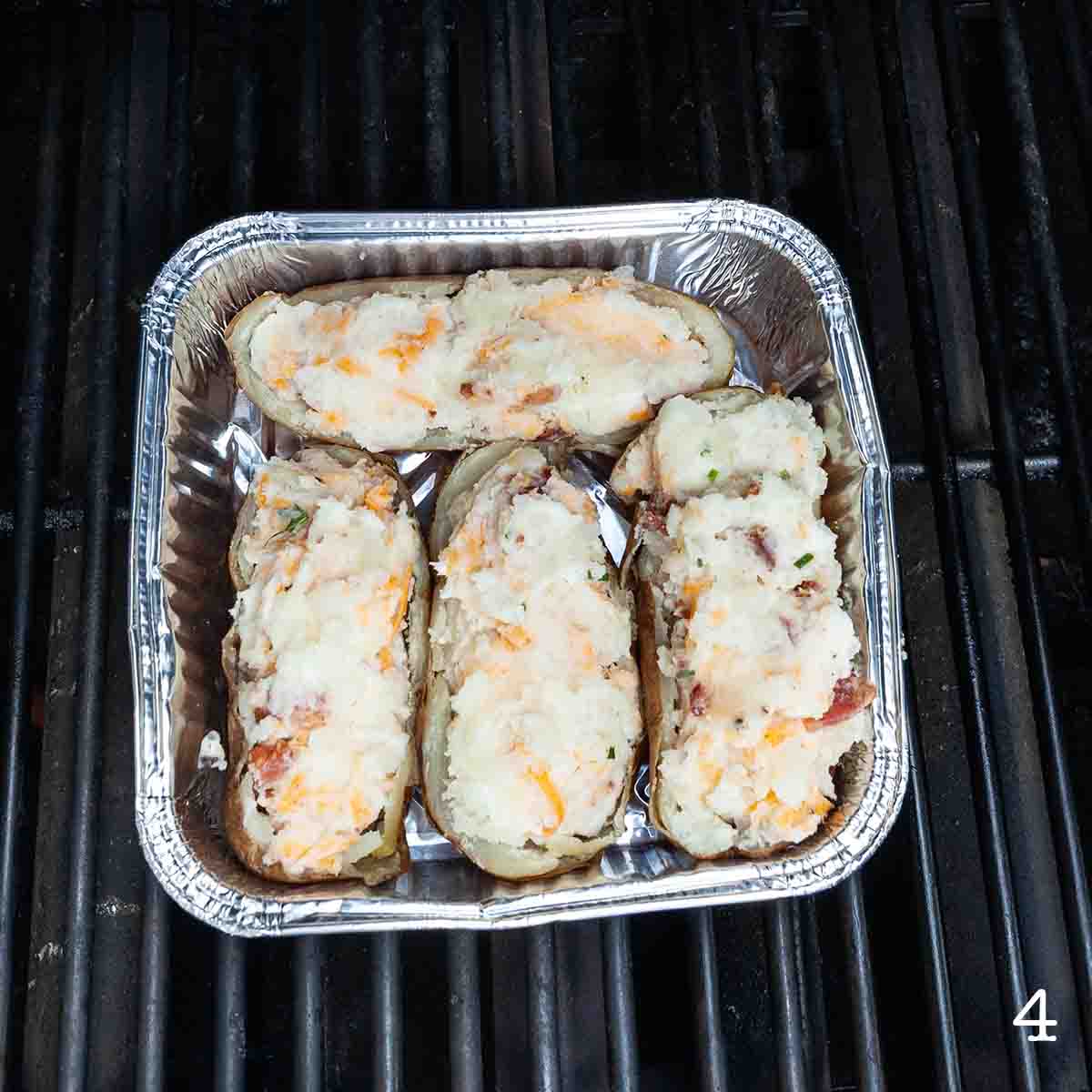 Four stuffed potato halves in a foil pan on the grill.