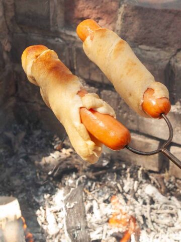 Two hot dogs wrapped in pastry over a campfire.