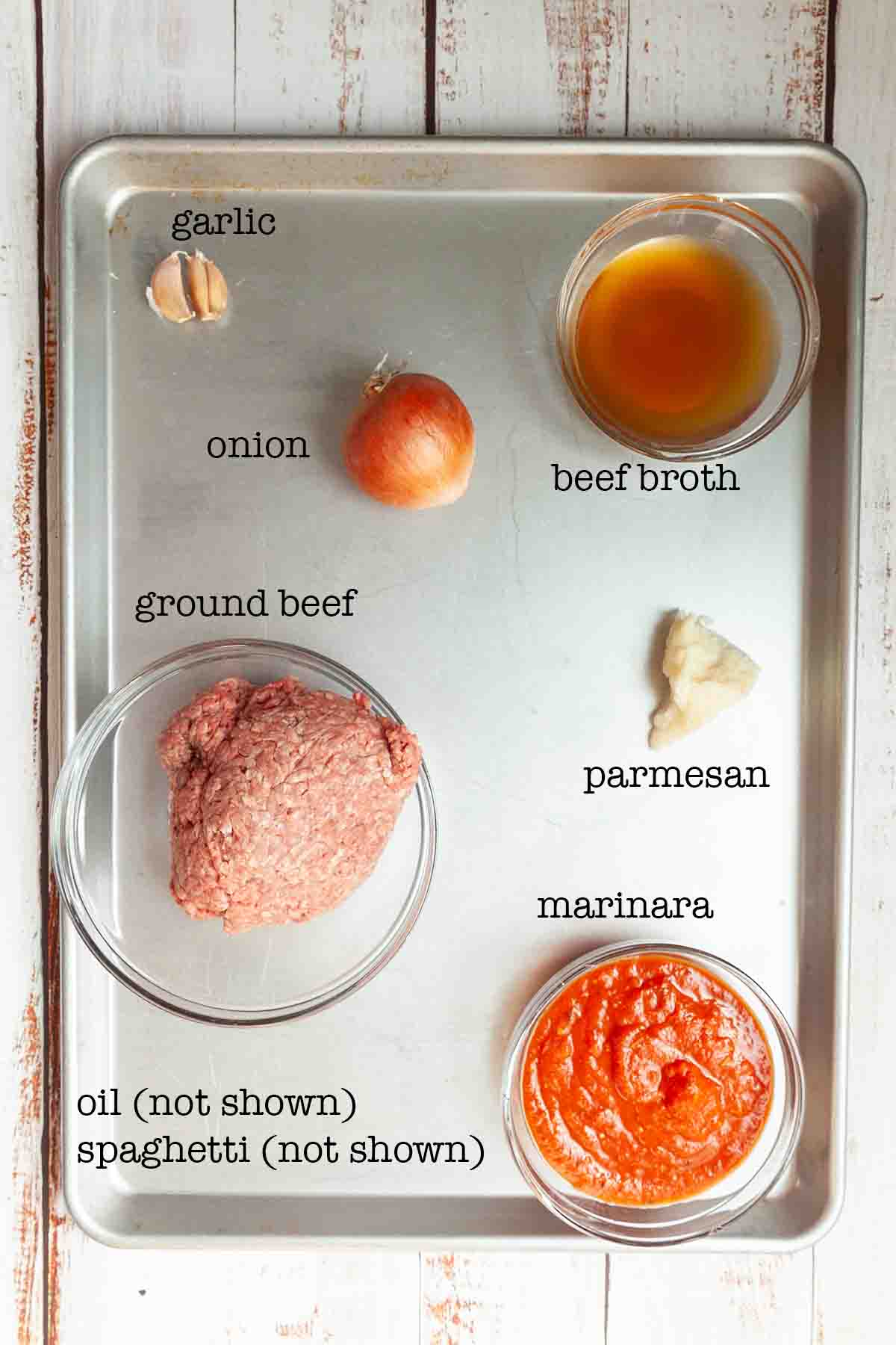 Ingredients for Dutch oven spaghetti--garlic, onion, beef broth, ground beef, parmesan, marinara, oil, and spaghetti.