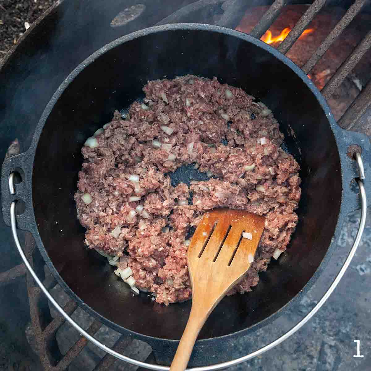 Ground beef and onion cooking in a Dutch oven over a campfire.
