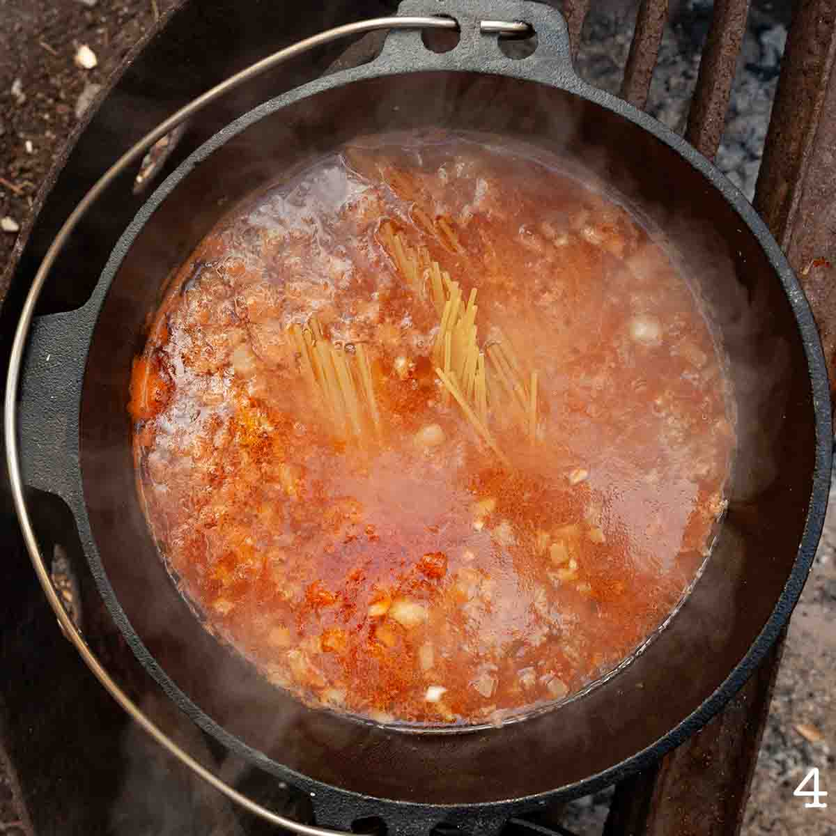 Spaghetti submerged in liquid in a Dutch oven over a campfire.