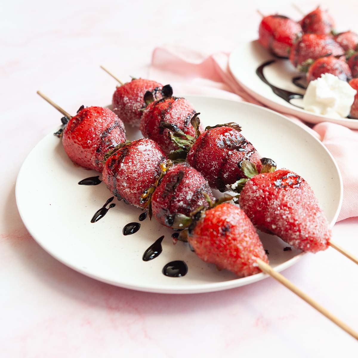 Skewers of grilled strawberries on a plate, drizzled with dark syrup.