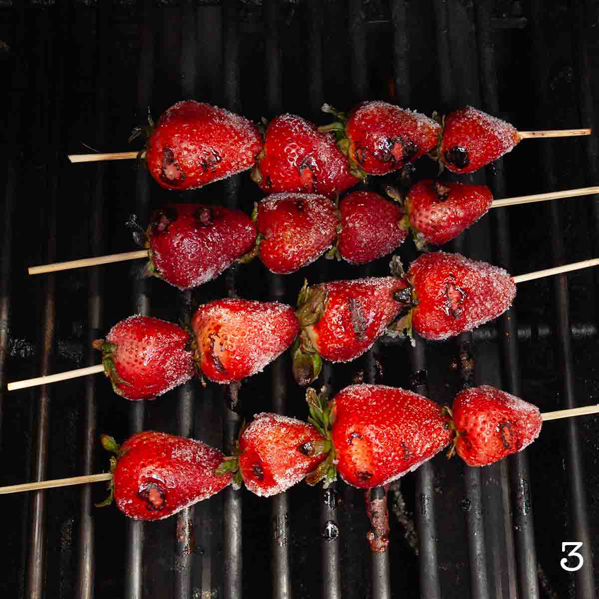 Four skewers of sugared strawberries on a grill.