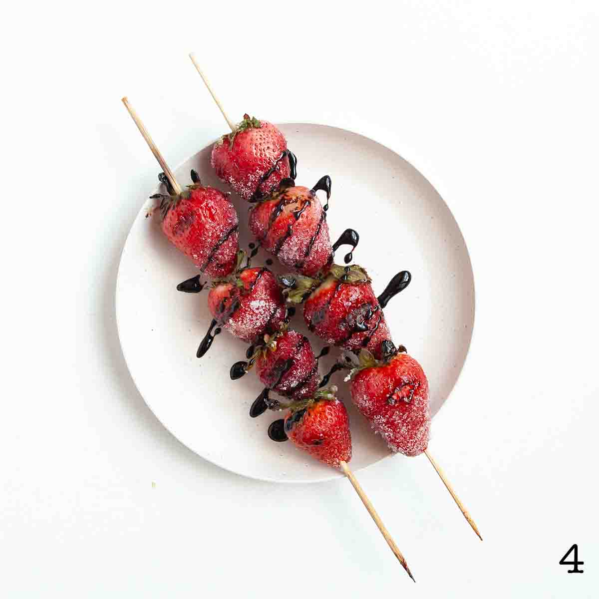 Two skewers of strawberries on a plate, drizzled with dark syrup.