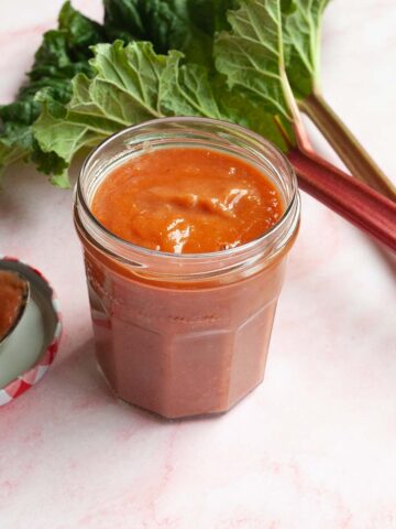 A jar of rhubarb bbq sauce with rhubarb stalks in the background.