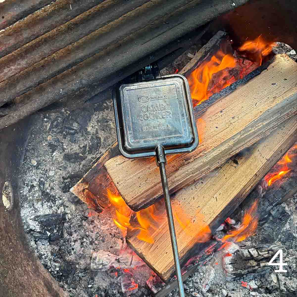 A campfire pie iron cooking over open flame.