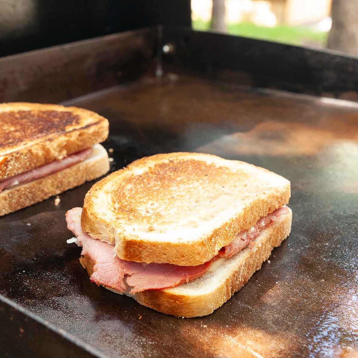 Two reuben sandwiches cooking on a Blackstone griddle.