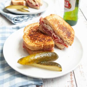 A grilled reuben sandwich on a plate with two pickle spears.