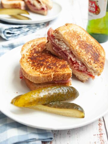A grilled reuben sandwich on a plate with two pickle spears.
