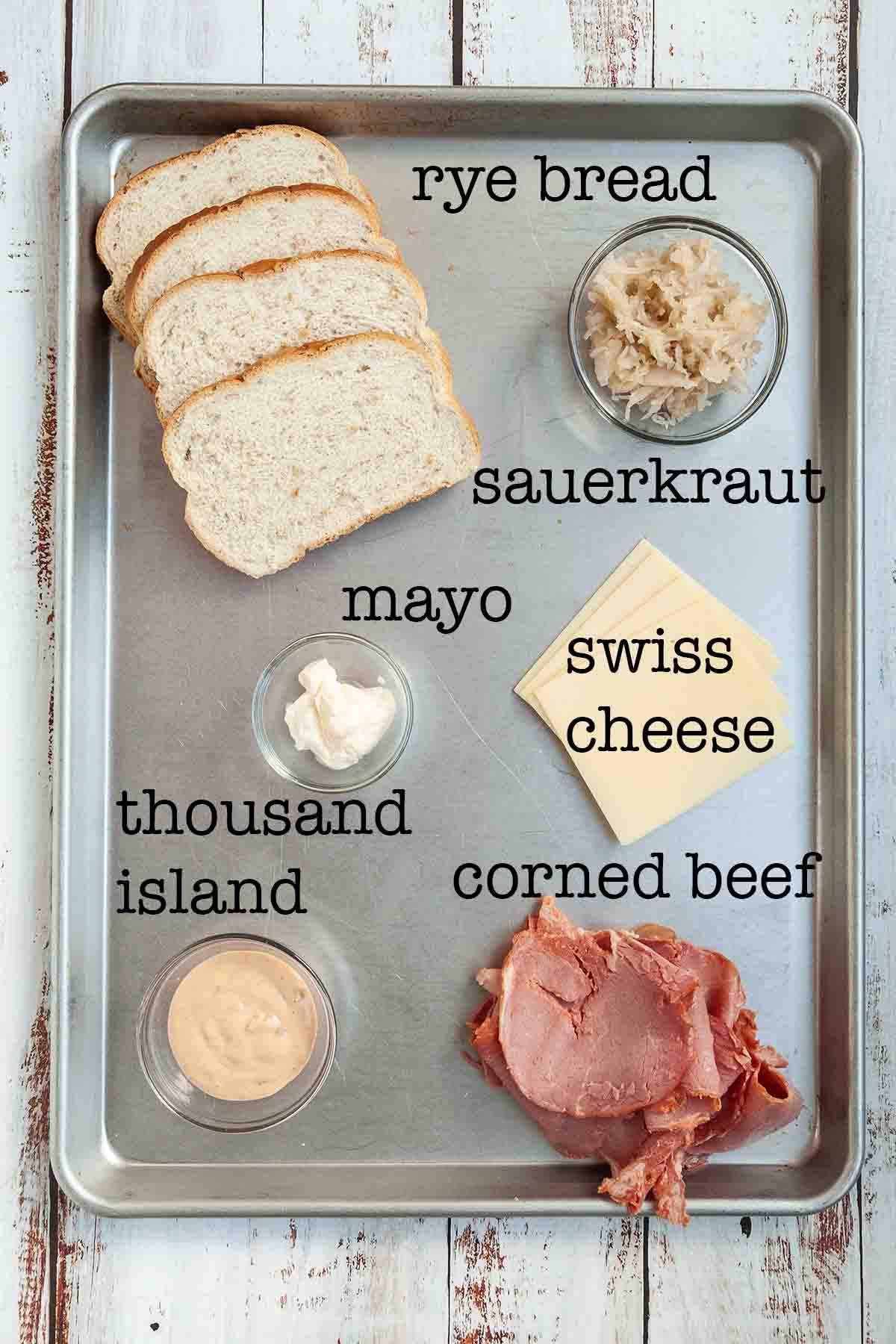 Ingredients for grilled reuben sandwich--rye bread, sauerkraut, mayo, swiss cheese, thousand island, and corned beef.
