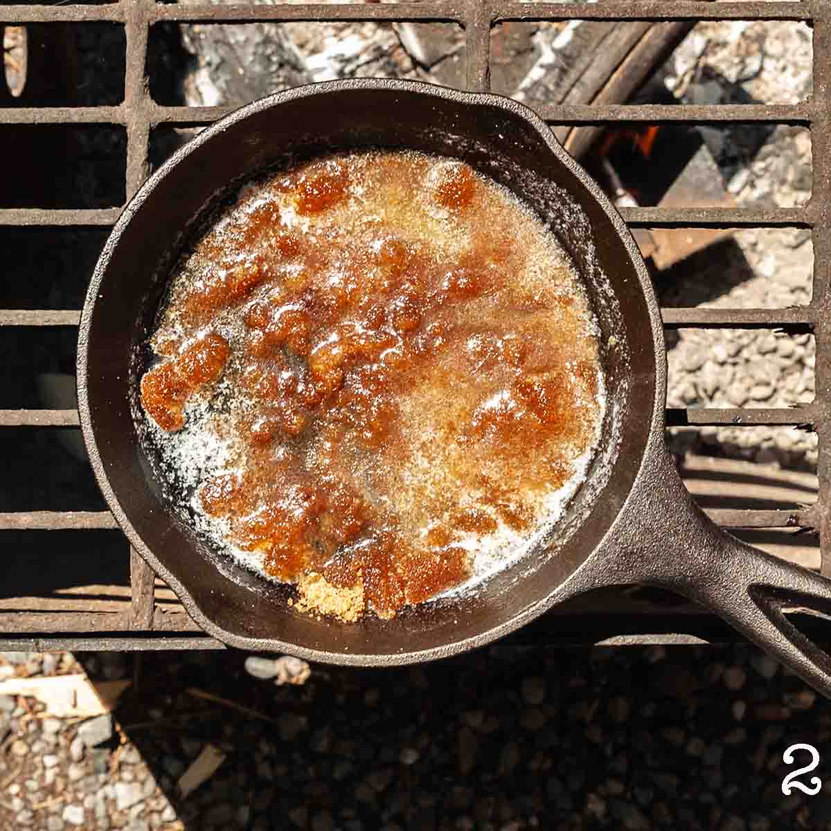 A brown sugar and butter mixture melting in a skillet over a fire.