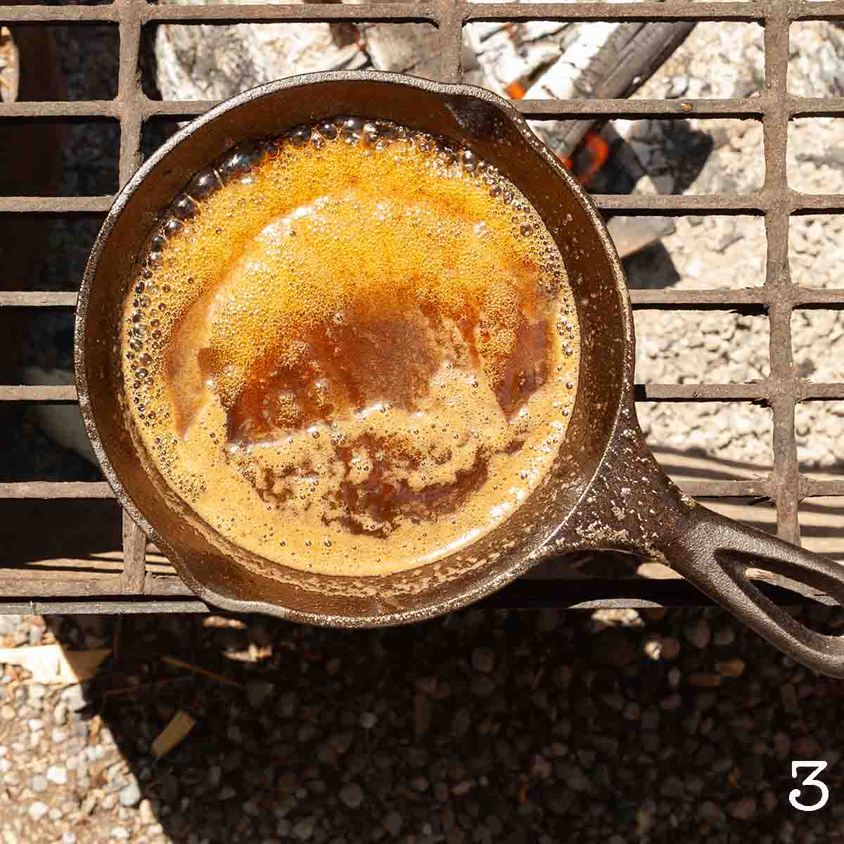 A brown sauce bubbling in a skillet over a fire.