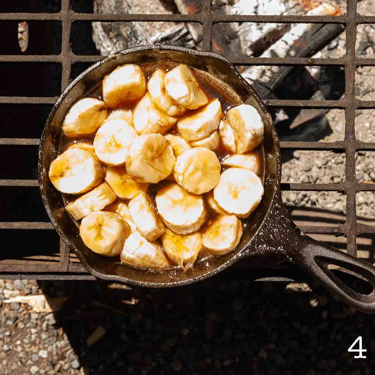 Bananas cooking in a sauce over a fire.