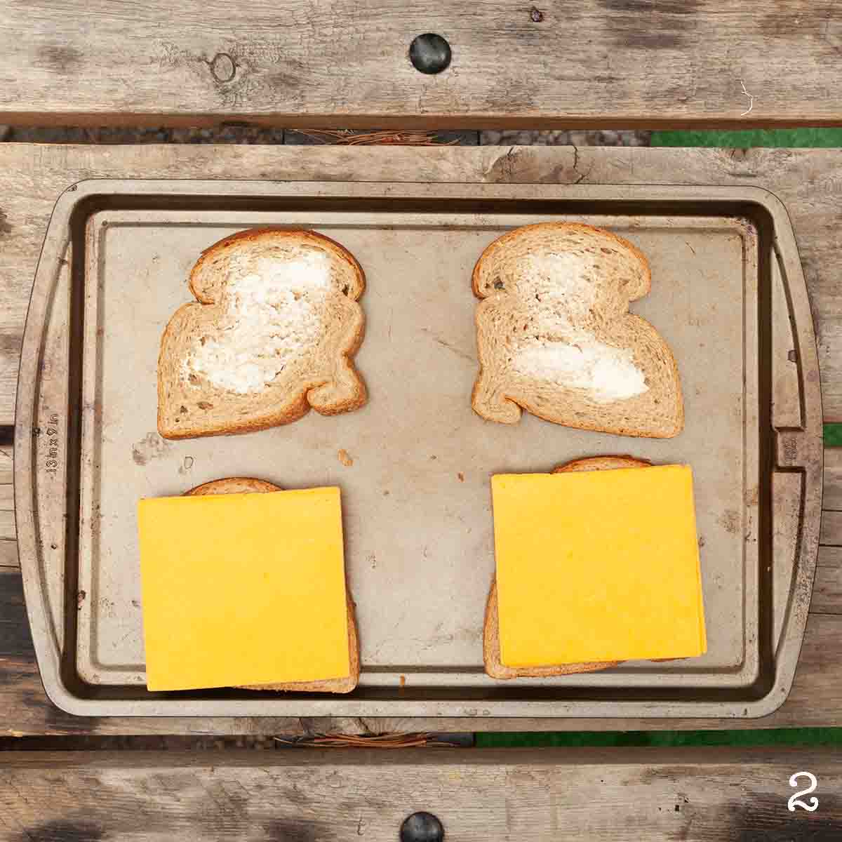 Four slices of buttered bread, with slices of cheese on top of two of the bread slices.