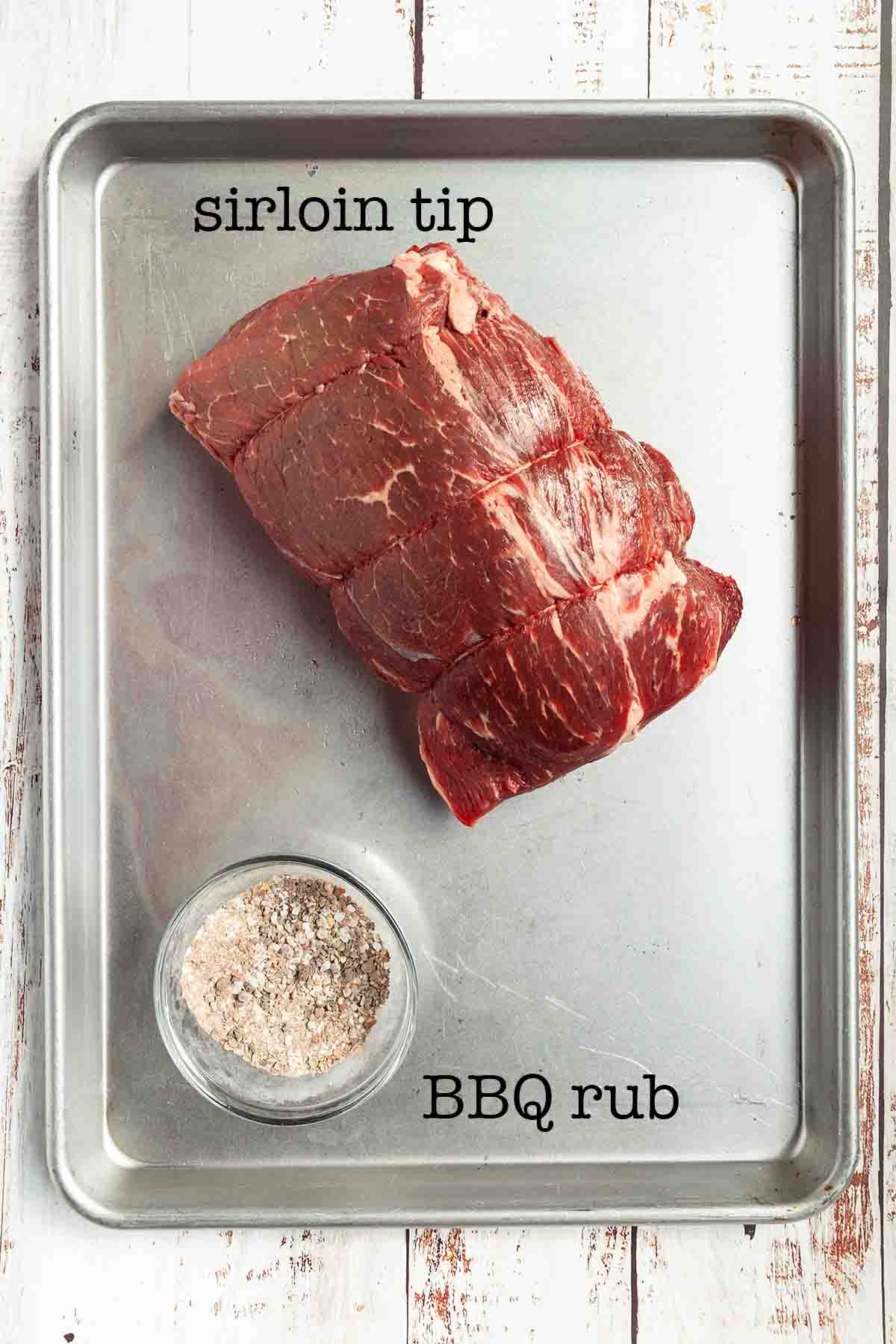 A sheet pan with a raw sirloin tip roast and a bowl of bbq rub.
