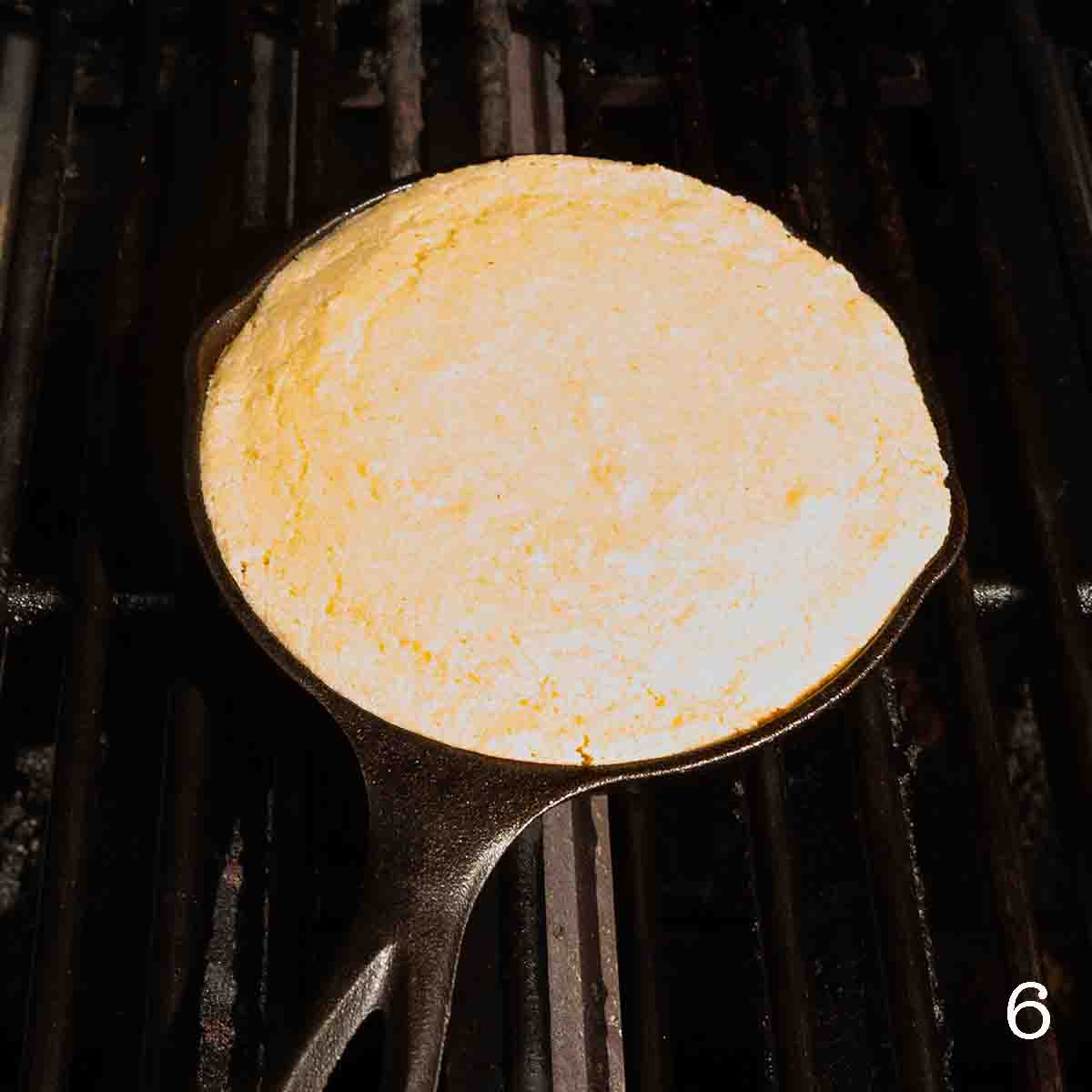 Cornbread cooking in a cast iron skillet on a grill.