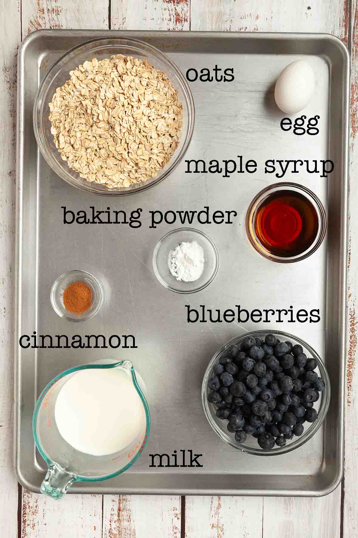 Ingredients for baked oatmeal--oats, egg, maple syrup, baking powder, cinnamon, milk, and blueberries.