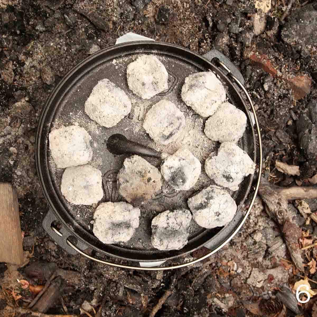 A Dutch oven covered in hot coals.