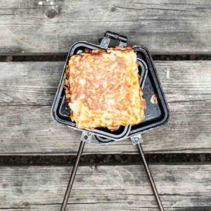 A pie iron hash brown patty resting on an open pie iron.