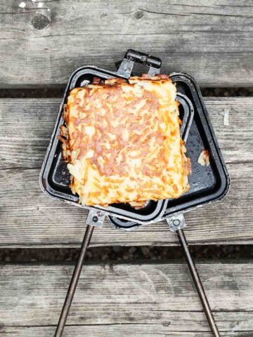 A pie iron hash brown patty resting on an open pie iron.