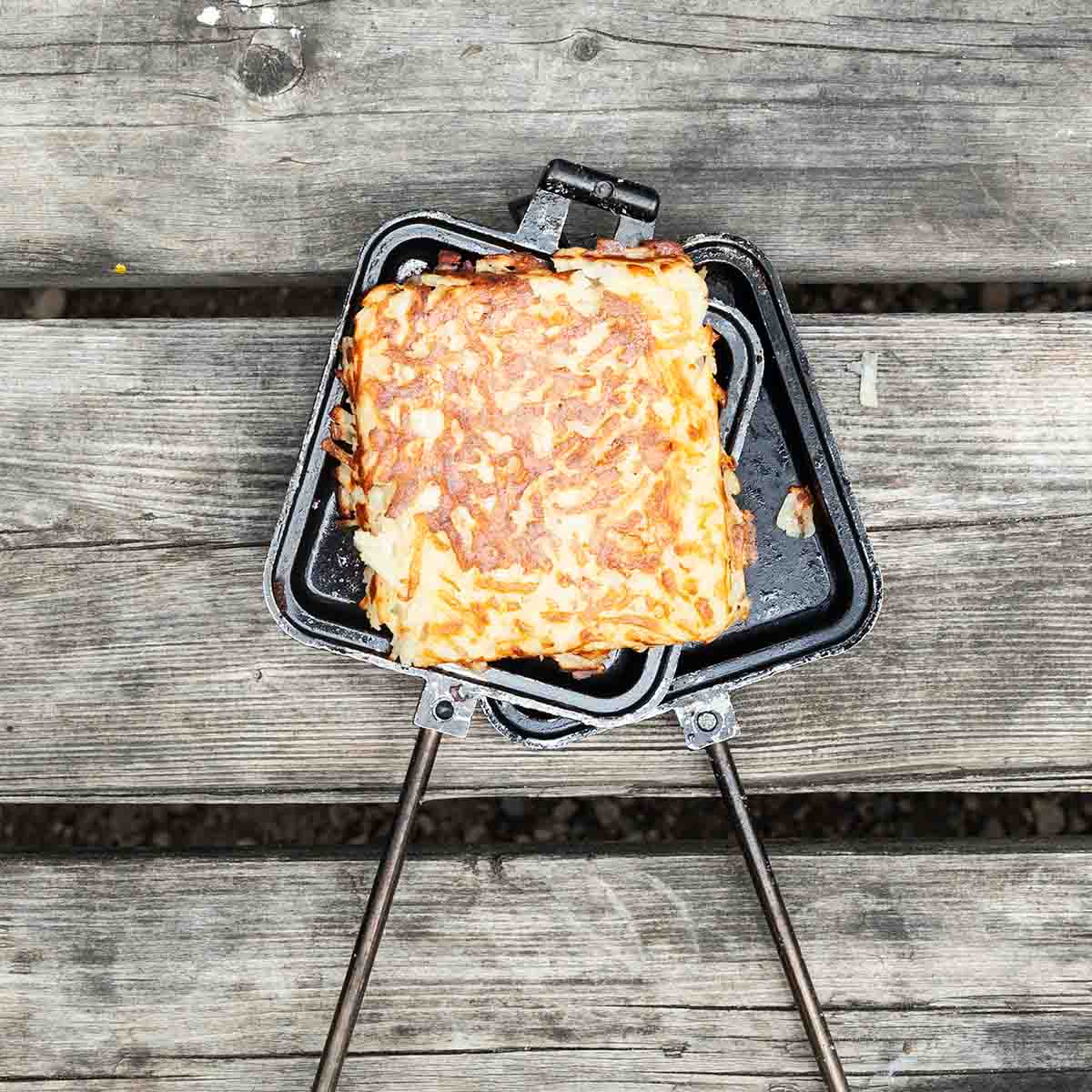 A pie iron hash brown patty resting on an open pie iron.