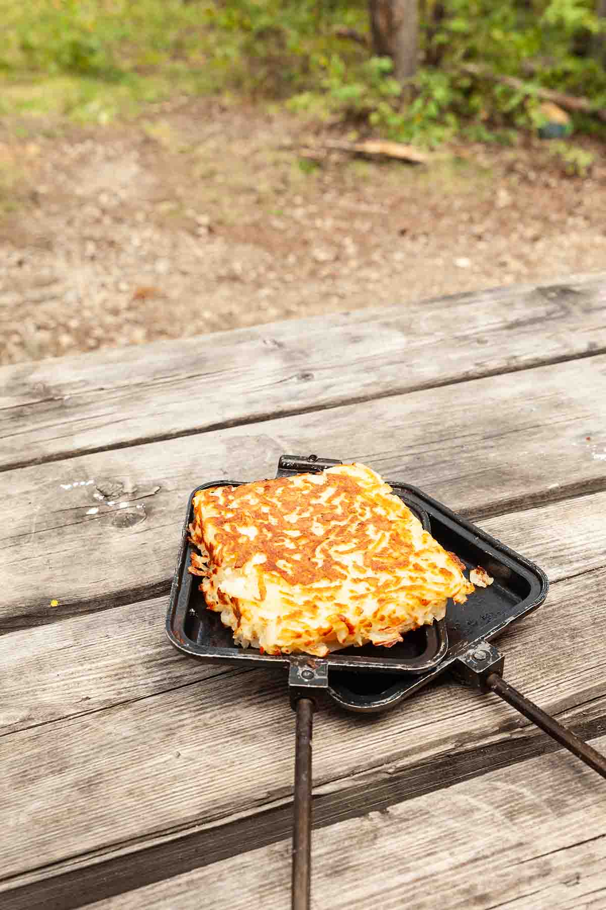 A pie iron hash brown patty resting on an open pie iron.