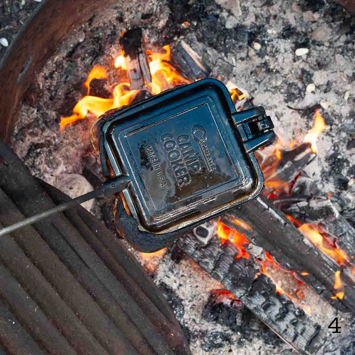A pie iron cooking over a campfire.