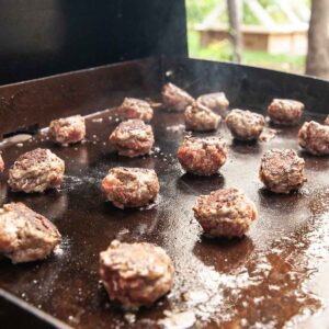 Meatballs cooking on an outdoor griddle.