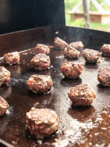 Meatballs cooking on an outdoor griddle.
