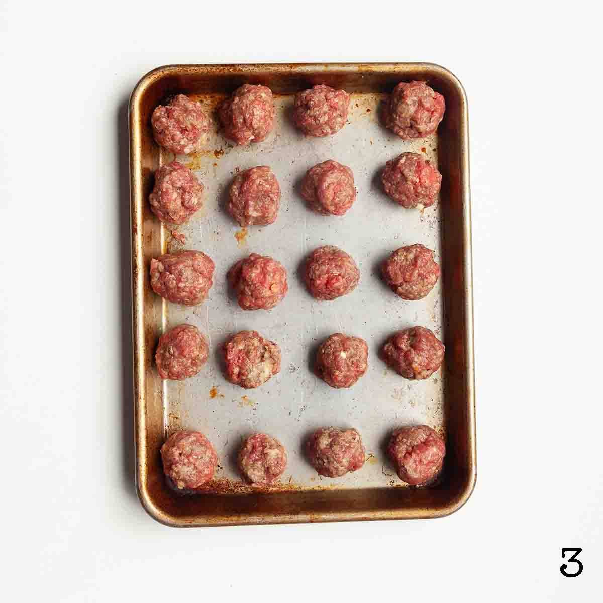 Twenty four shaped uncooked meatballs on a baking sheet.