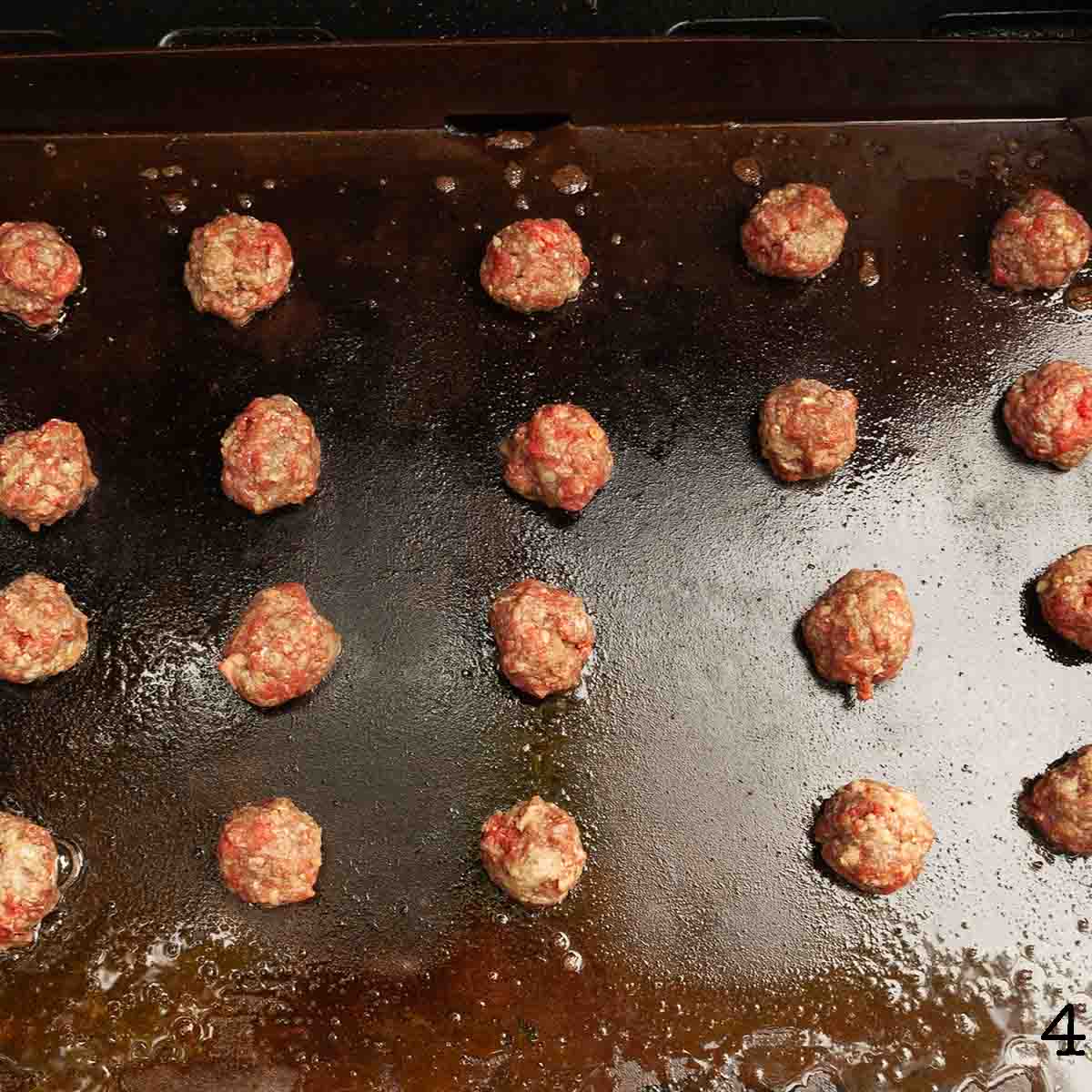 Meatballs cooking on an outdoor griddle.