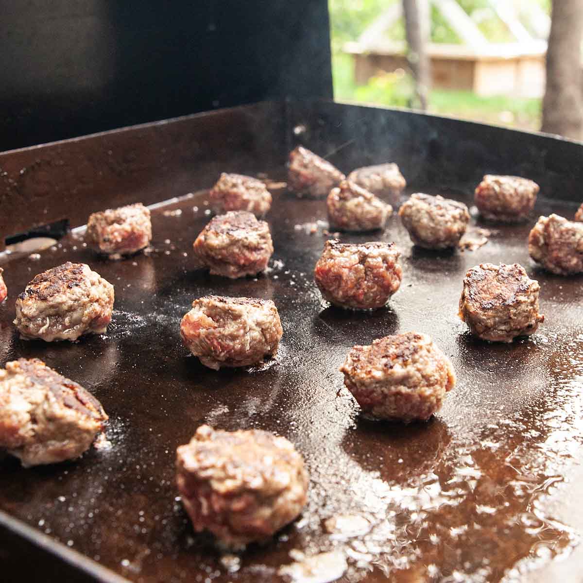 Meatballs cooking on an outdoor griddle.