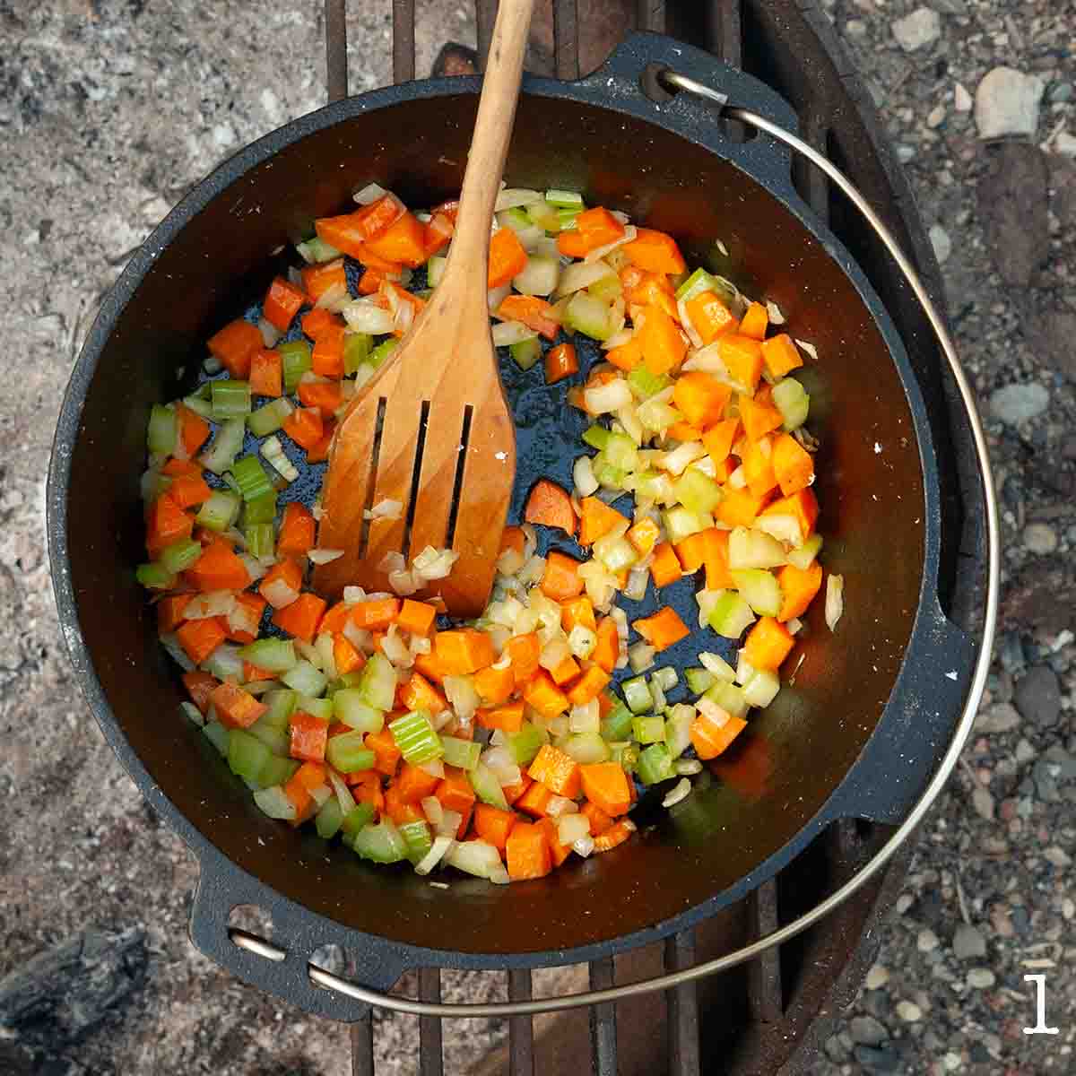 Celery, carrot, and onion cooking in a Dutch oven over a campfire.