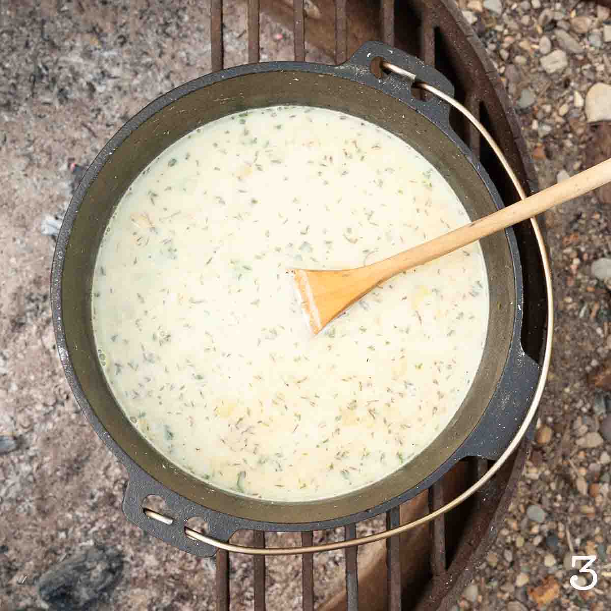 A pot of creamy liquid over a campfire.