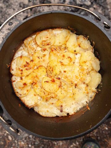 A Dutch oven filled with sliced potatoes and melted cheese.