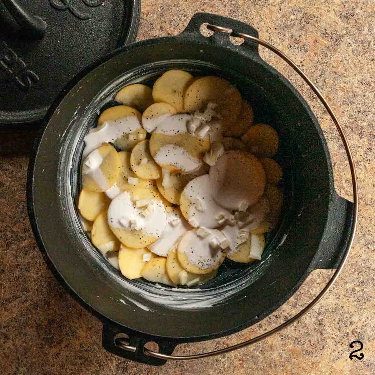 Potatoes, diced onion, and cream layered in a Dutch oven.