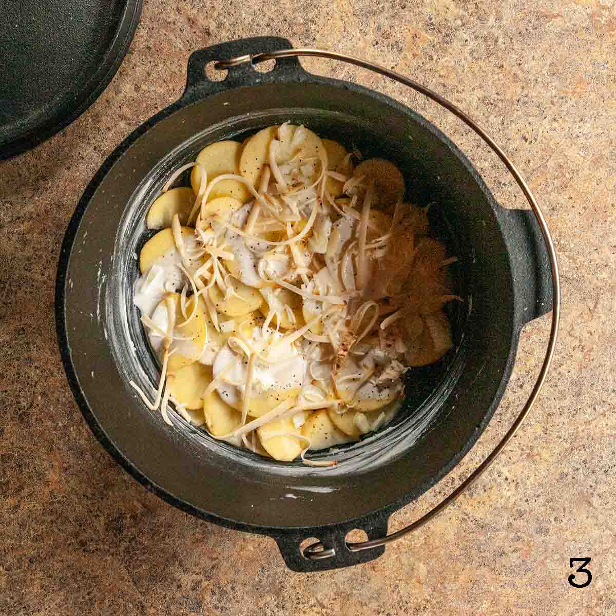Potatoes, onion, and cream topped with shredded cheese in a Dutch oven.