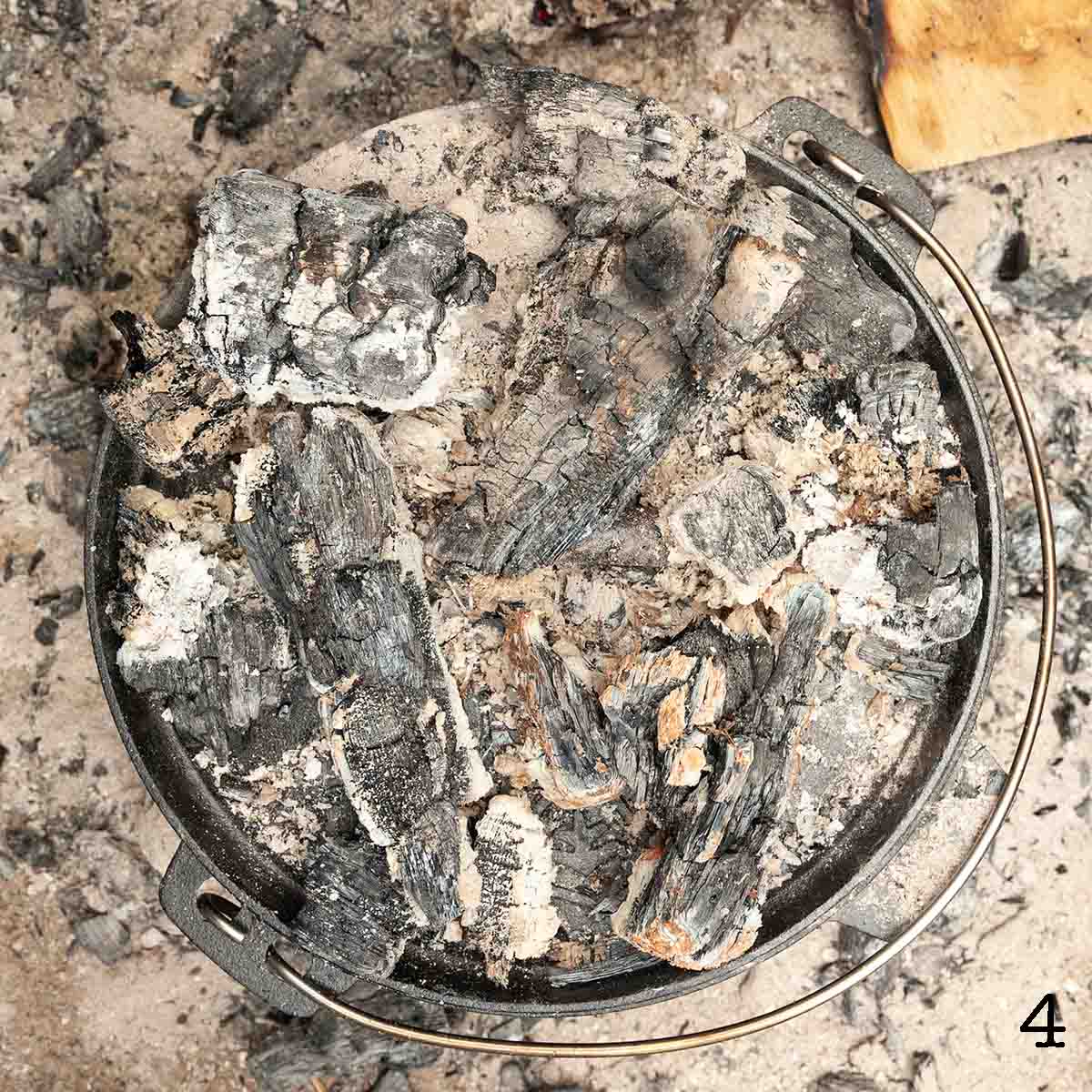 A Dutch oven covered with fire embers.